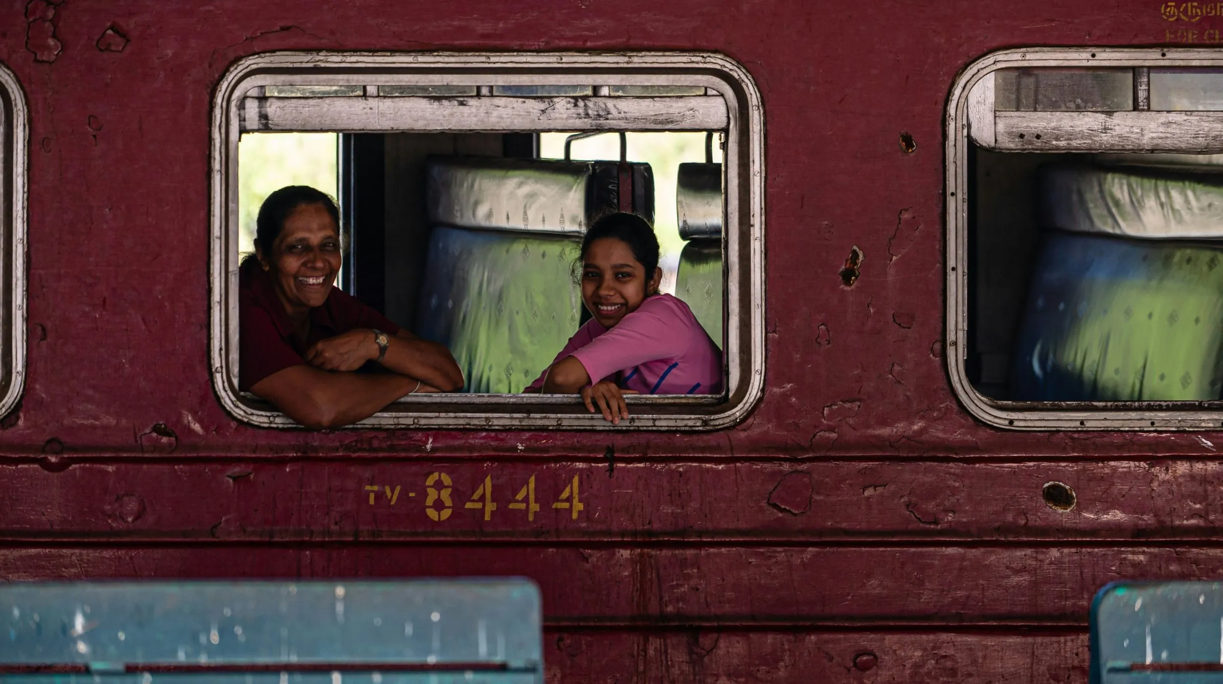 Voyageurs regardant par la fenêtre d’un train rouge au Sri Lanka, immersion authentique en train local.