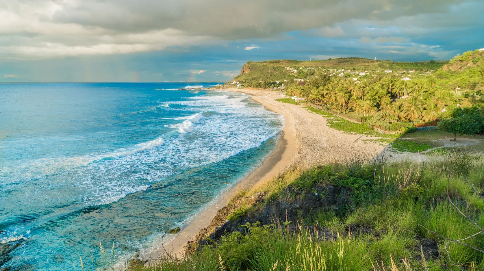 Plage de boucan canon, paisible bordée de palmiers et d'eaux turquoise sous un ciel nuageux sur l'île de la Réunion.