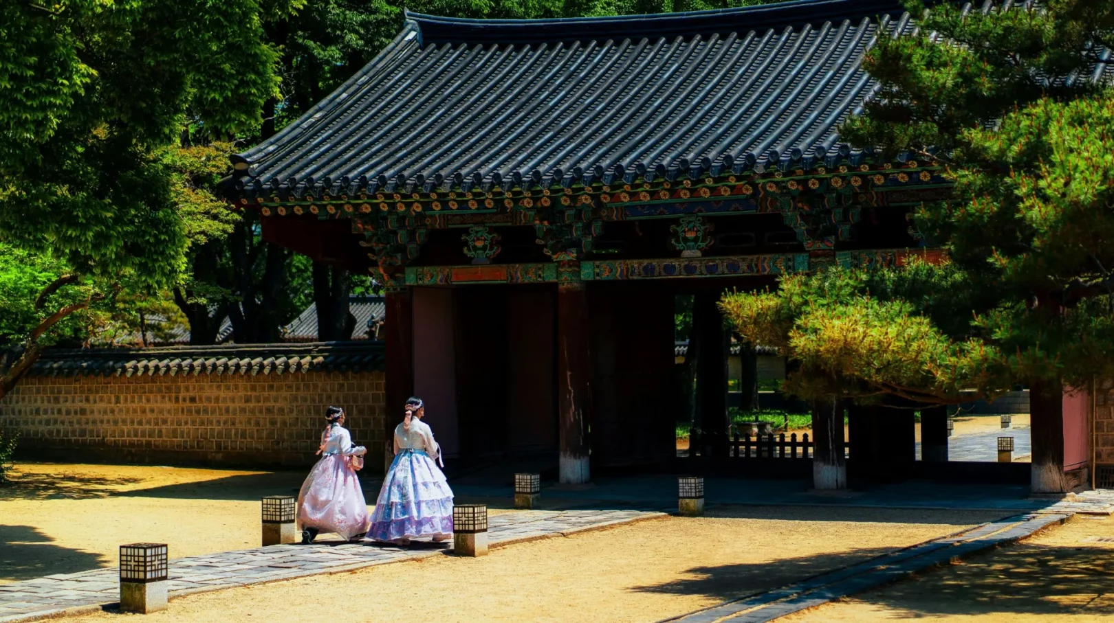 Deux femmes en hanbok traditionnel coréen marchant devant la porte en bois ornée du palais Deoksugung à Séoul, Corée du Sud