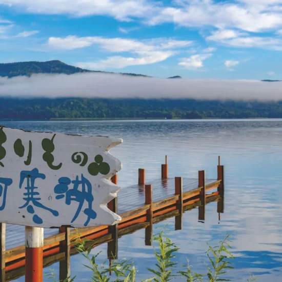 Lac paisible entouré de montagnes, avec un ponton en bois et des nuages bas.
