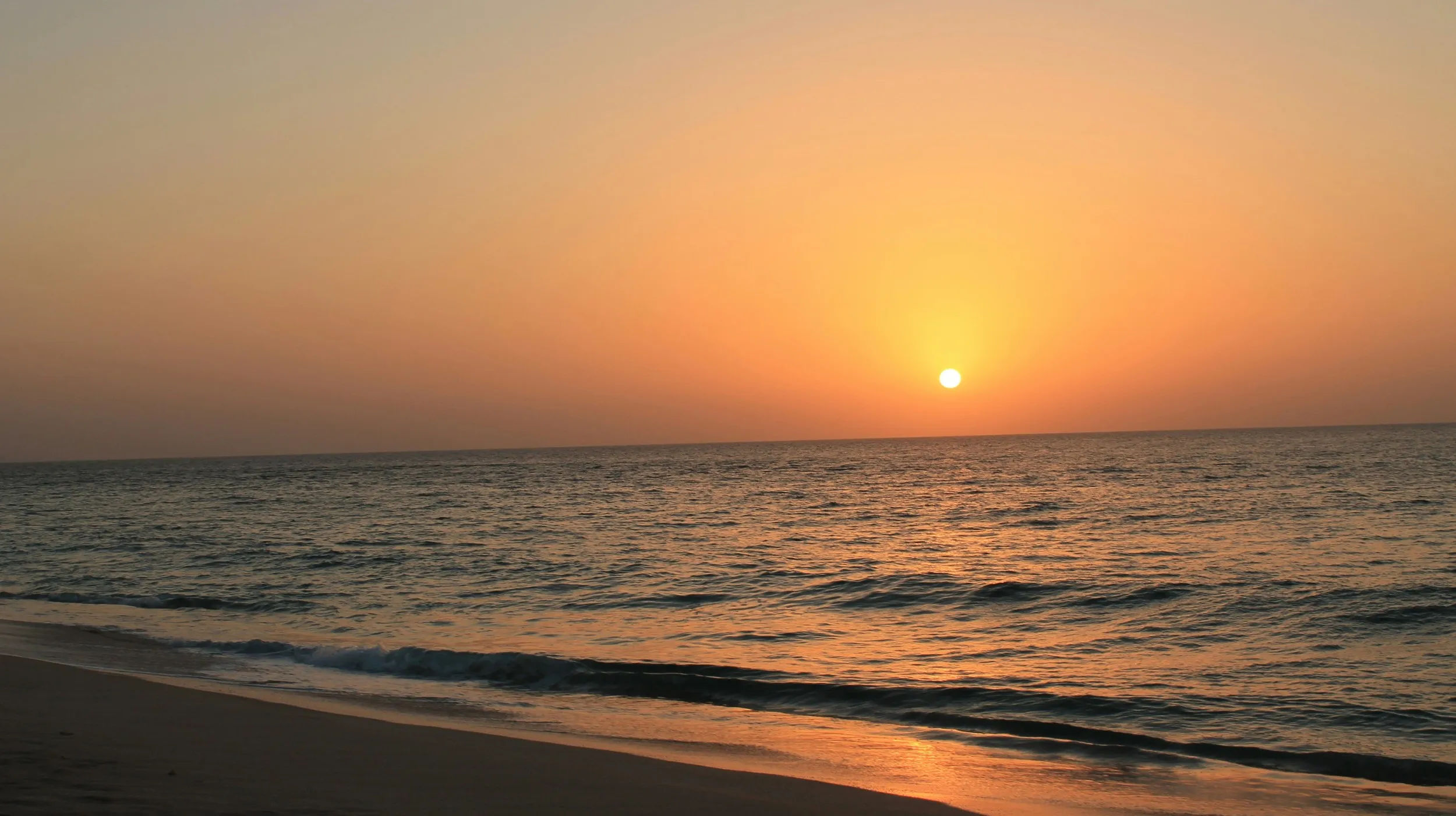 Coucher de soleil sur une plage paisible à Oman, illuminant l'horizon d'une lumière dorée.