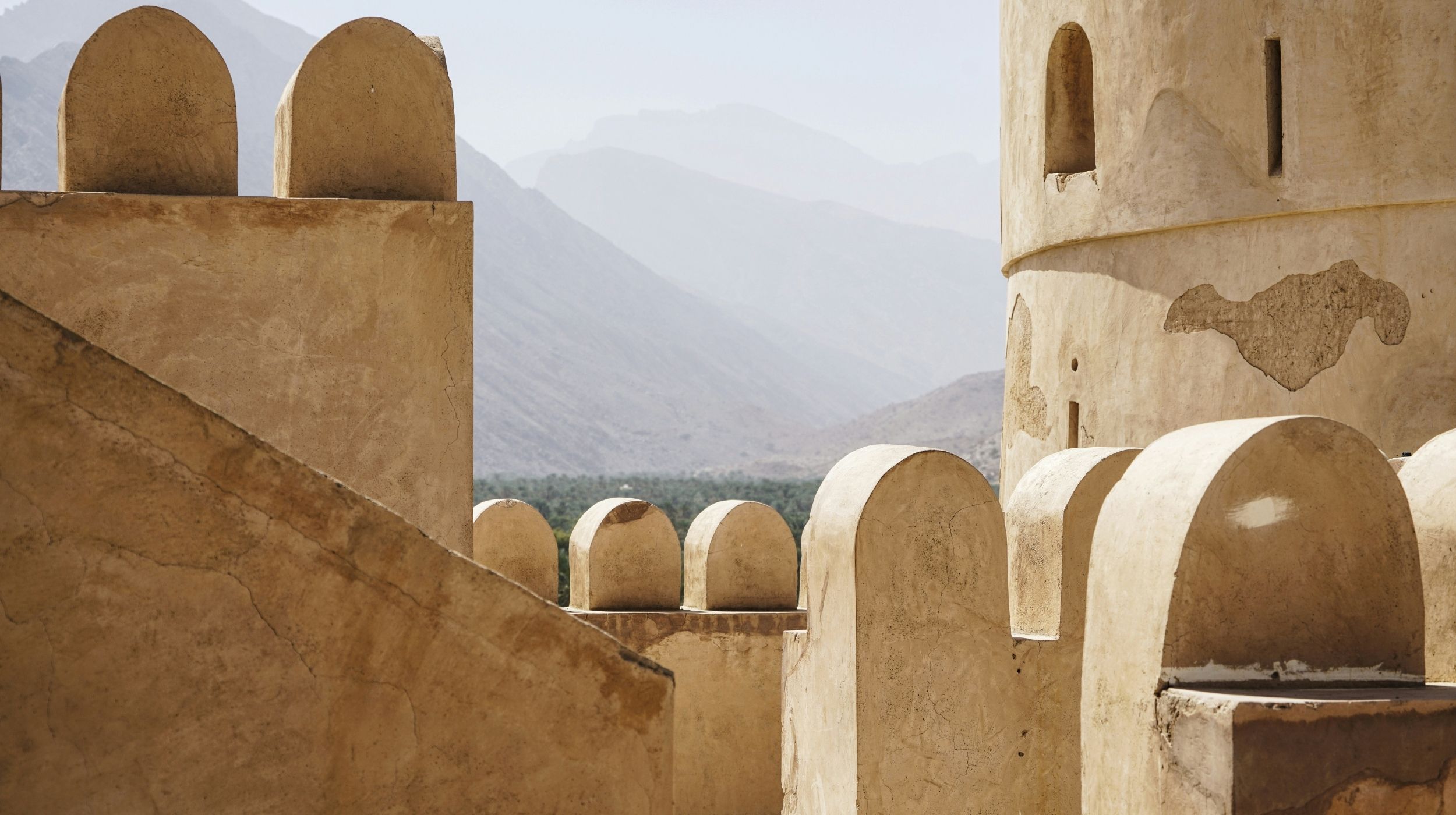 Architecture traditionnelle omanaise dans un fort en terre, avec vue sur les montagnes du Hajar – symbole du patrimoine historique d’Oman.