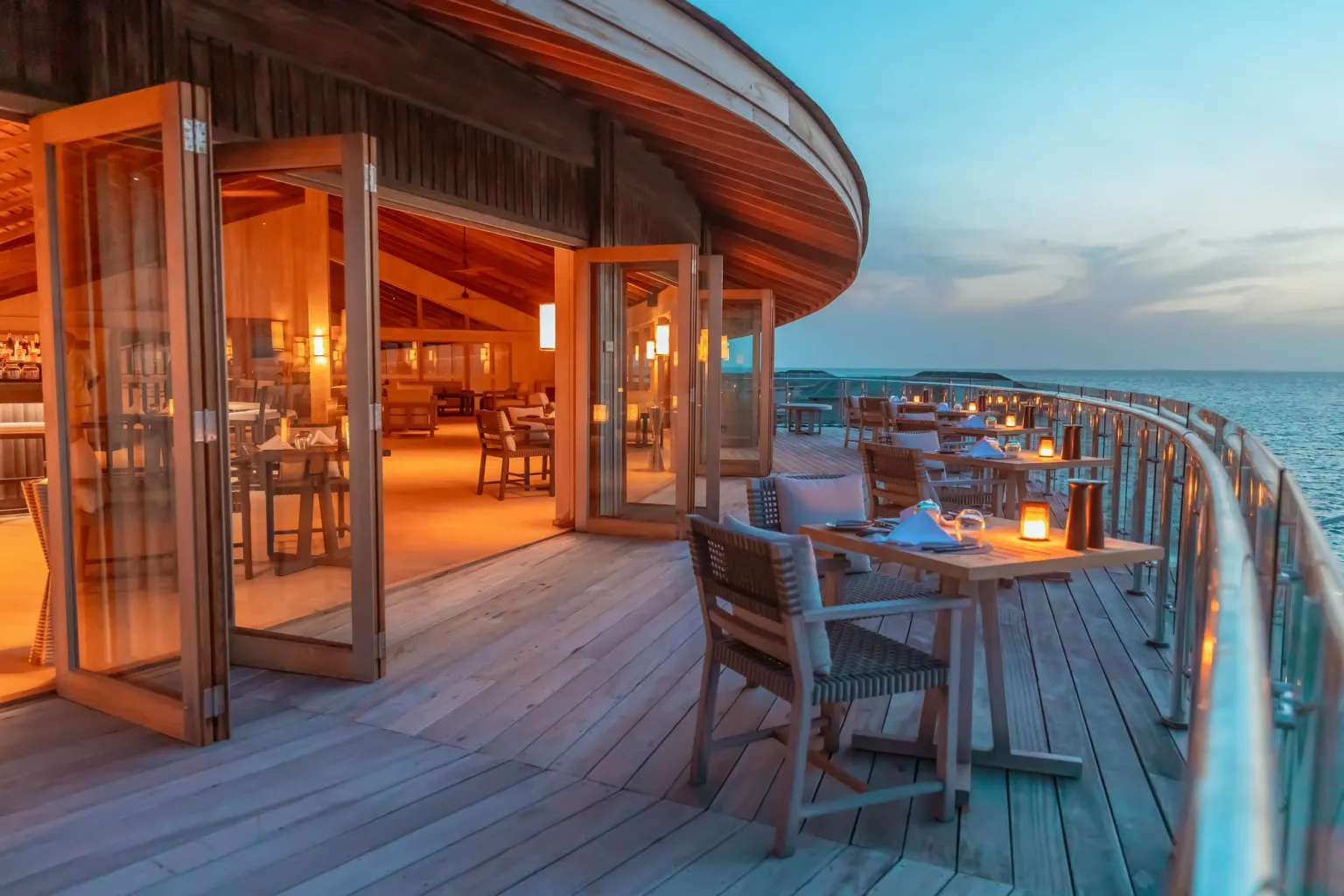 Terrasse en bois au bord de l'eau, éclairée par des lanternes, offrant une vue apaisante sur l'horizon.