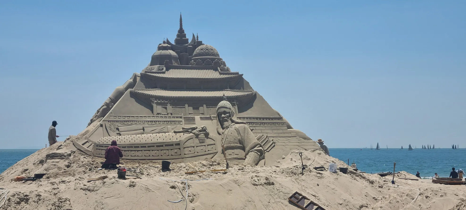 Plage ensoleillée — sculpture de sable impressionnante et créative, avec des artistes au travail.