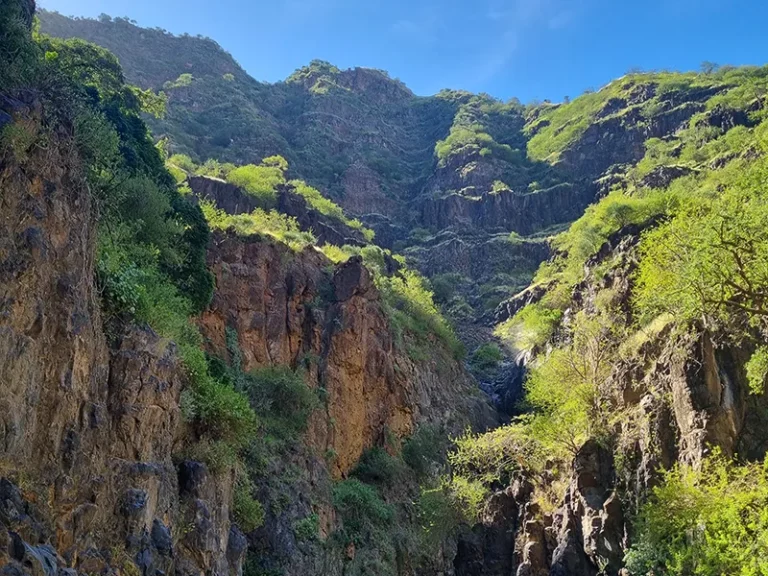 Un paysage spectaculaire de montagnes verdoyantes, avec des falaises majestueuses et un ciel bleu éclatant.