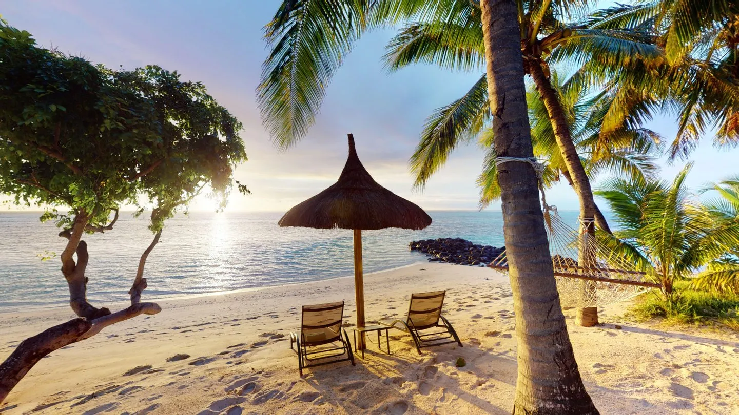 Paradise Beachcomber à Maurice - Plage paisible avec chaises longues et parasol, bordée de palmiers, offrant une vue sur l'océan scintillant.
