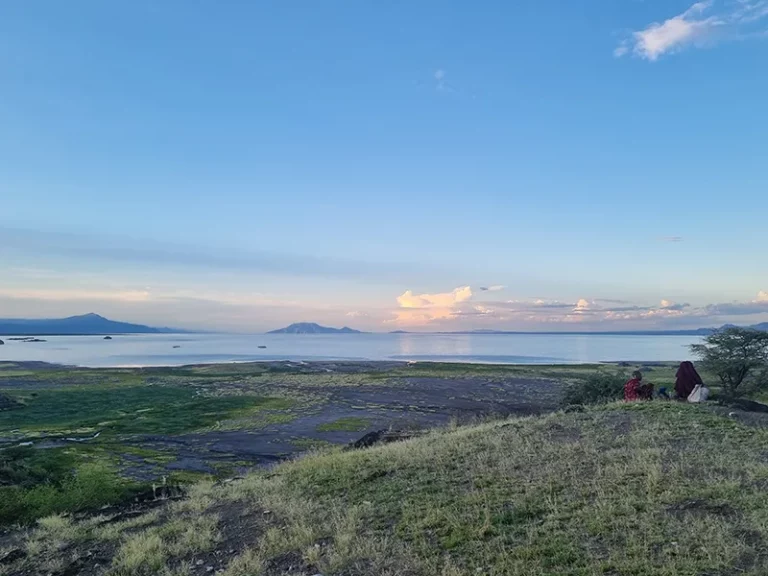 Paysage paisible avec vue sur un lac et des collines verdoyantes sous un ciel lumineux.