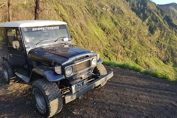 Véhicule tout-terrain sur une route pittoresque entourée de collines verdoyantes.