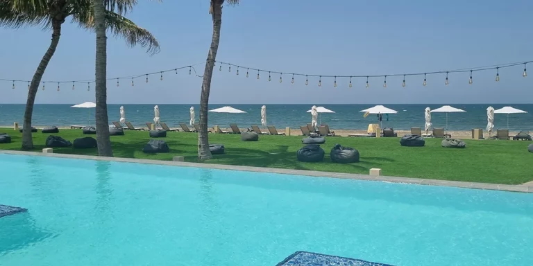 Plage ensoleillée avec piscine et chaises longues, ambiance paisible et tropicale.