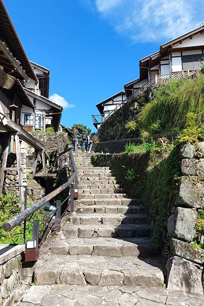 Escaliers en pierre bordés de maisons traditionnelles sous un ciel bleu éclatant, ambiance paisible et charmante.