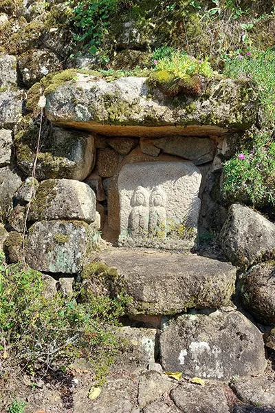 Élément sculpté dans un mur de pierre, entouré de verdure luxuriante et d'une ambiance paisible.