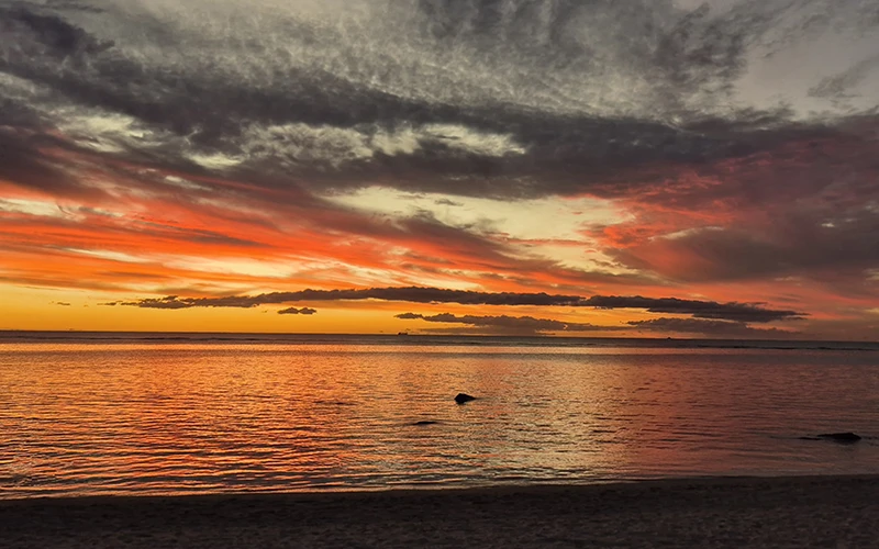 Coucher de soleil spectaculaire sur l'océan, illuminant le ciel de couleurs éclatantes.