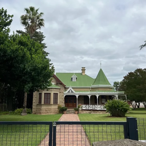 Maison historique avec un toit vert, entourée de verdure, offrant une ambiance tranquille et charmante.