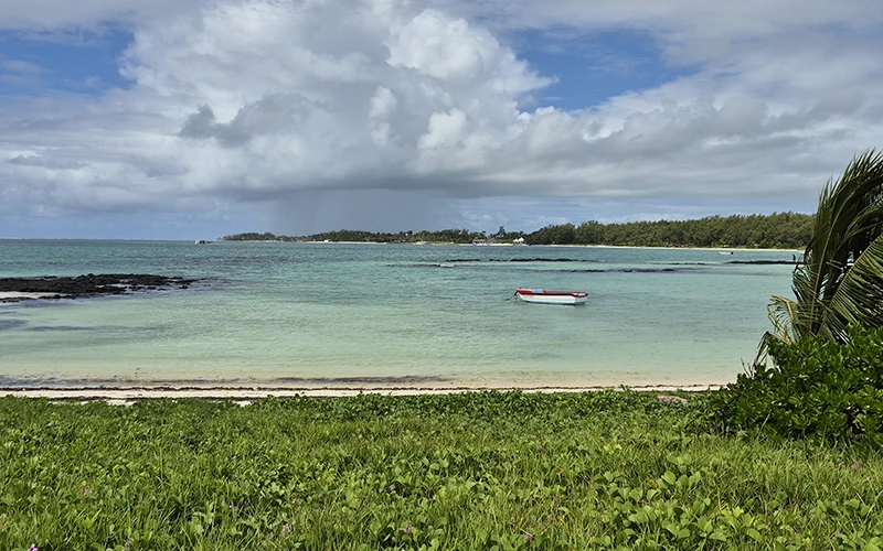 Île Maurice — Plage paisible avec un bateau rouge sur une mer turquoise entourée de verdure luxuriante.
