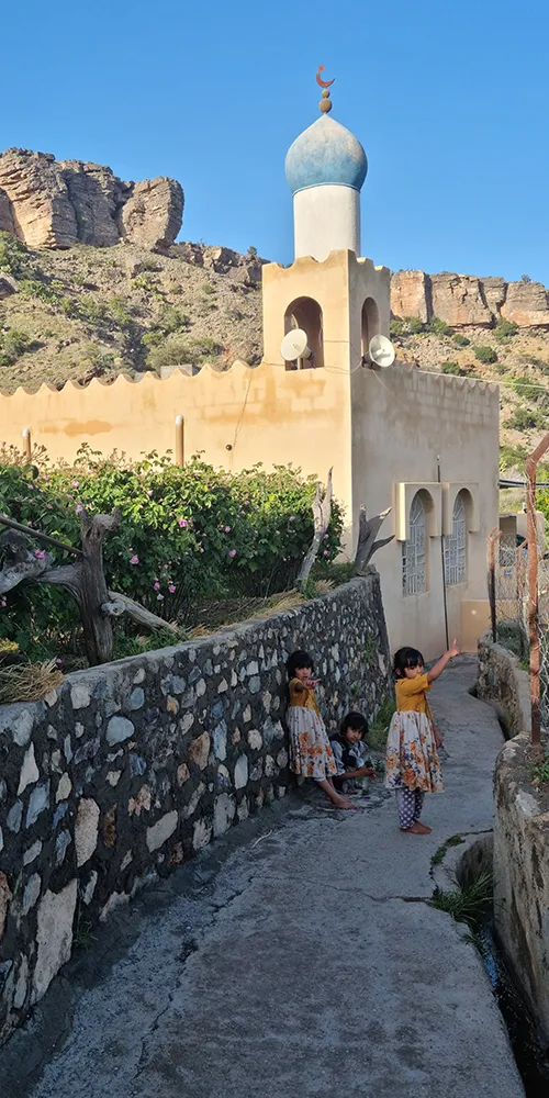 Village pittoresque — Enfants jouant devant une maison aux murs colorés et à la coupole bleue, entourés de montagnes.