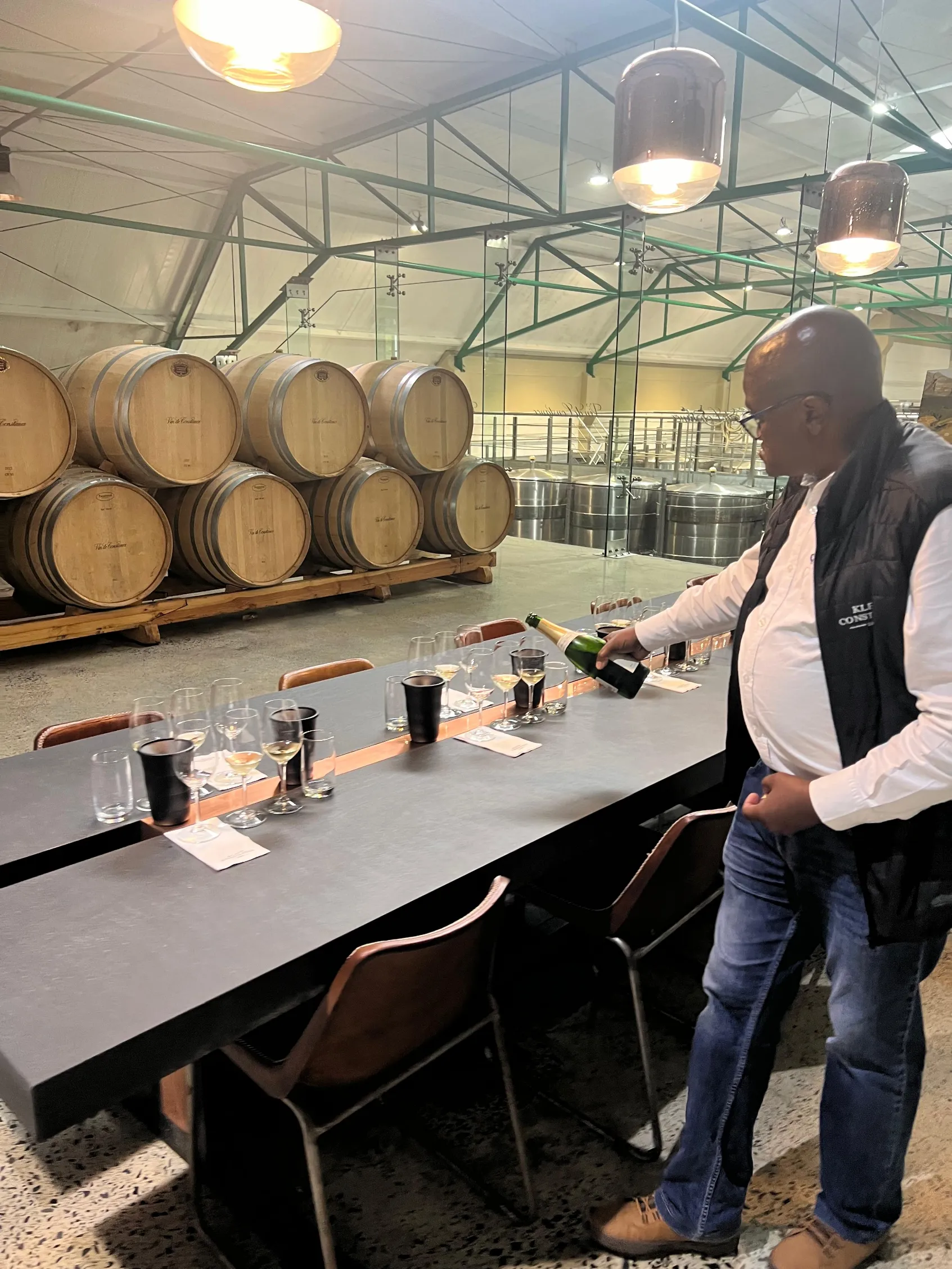 Dégustation de vin dans une cave sud africaine moderne avec des fûts en bois, ambiance conviviale et chaleureuse.