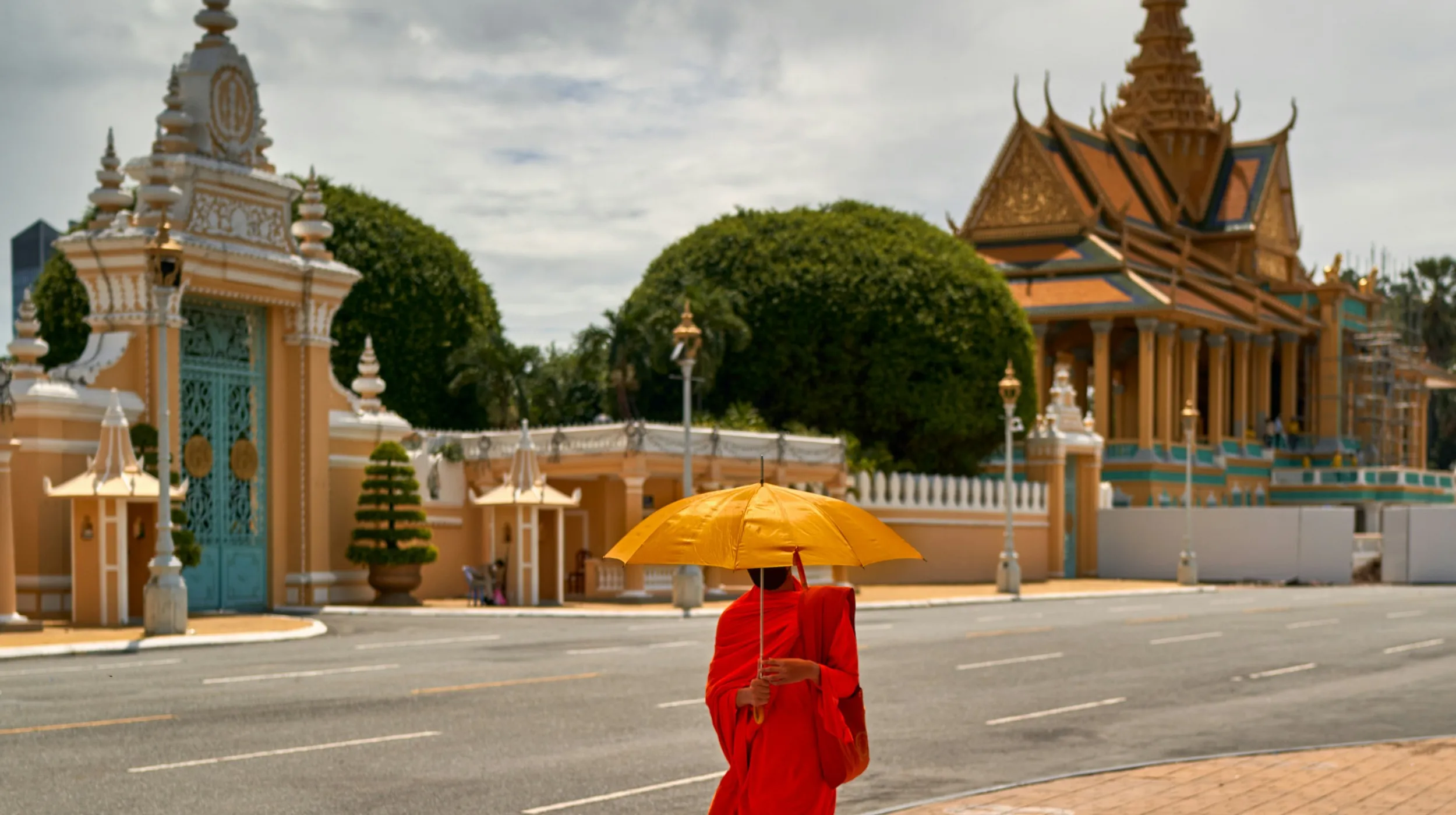 Moine en robe rouge sous un parapluie jaune, devant un temple coloré et majestueux.