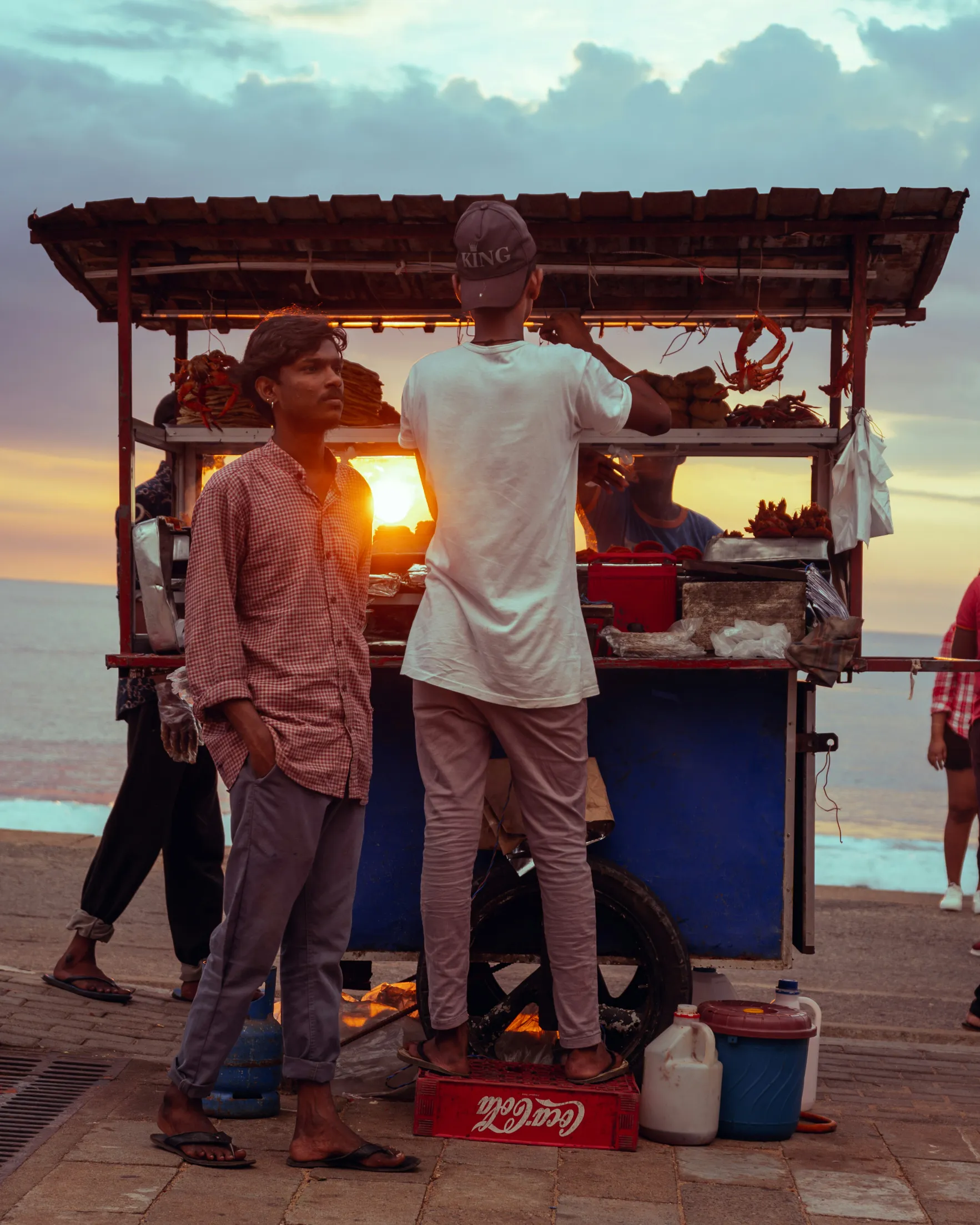 Scène animée au coucher de soleil, avec des vendeurs de rue et une ambiance conviviale au bord de l'océan.