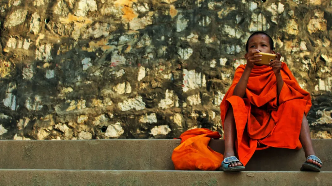 Enfant en robe orange, assis sur des marches, absorbé par son téléphone, devant un mur texturé.