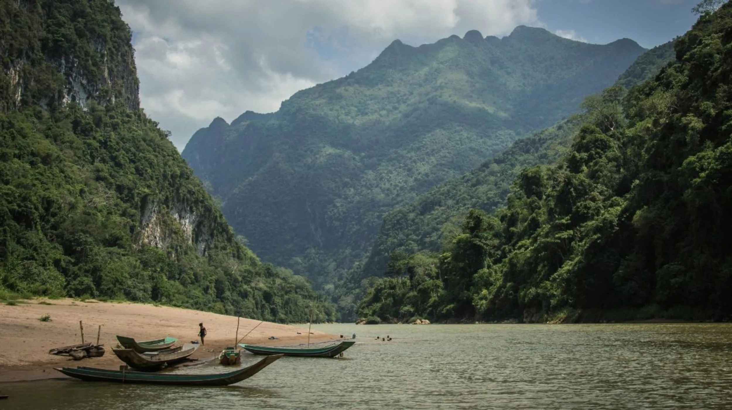 Rivière paisible bordée de montagnes luxuriantes et de barques traditionnelles, offrant un paysage enchanteur.