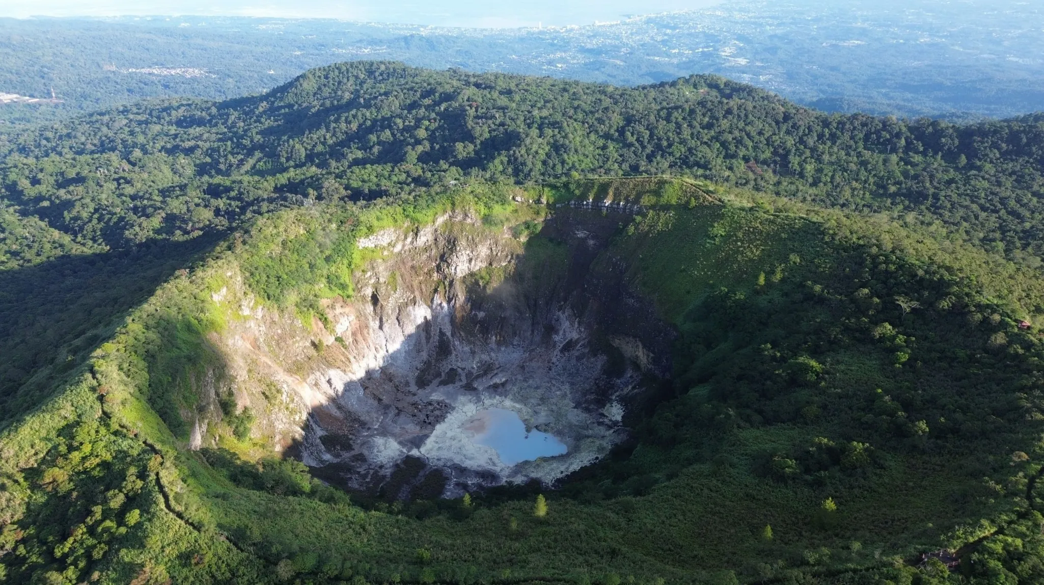 Vaste cratère verdoyant entouré de montagnes luxuriantes et d'une eau turquoise, un spectacle naturel époustouflant.