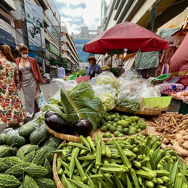 Marché animé, Thaïlande — étals colorés de légumes frais sous un parasol rouge.