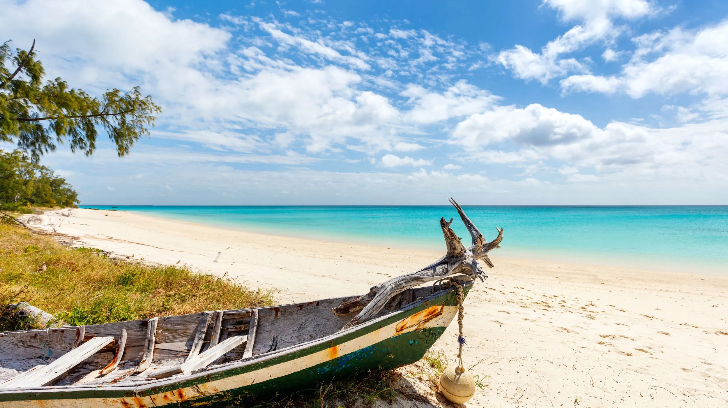 Plage paisible avec un bateau de pêche en bois, bordée par une mer turquoise et un ciel lumineux.