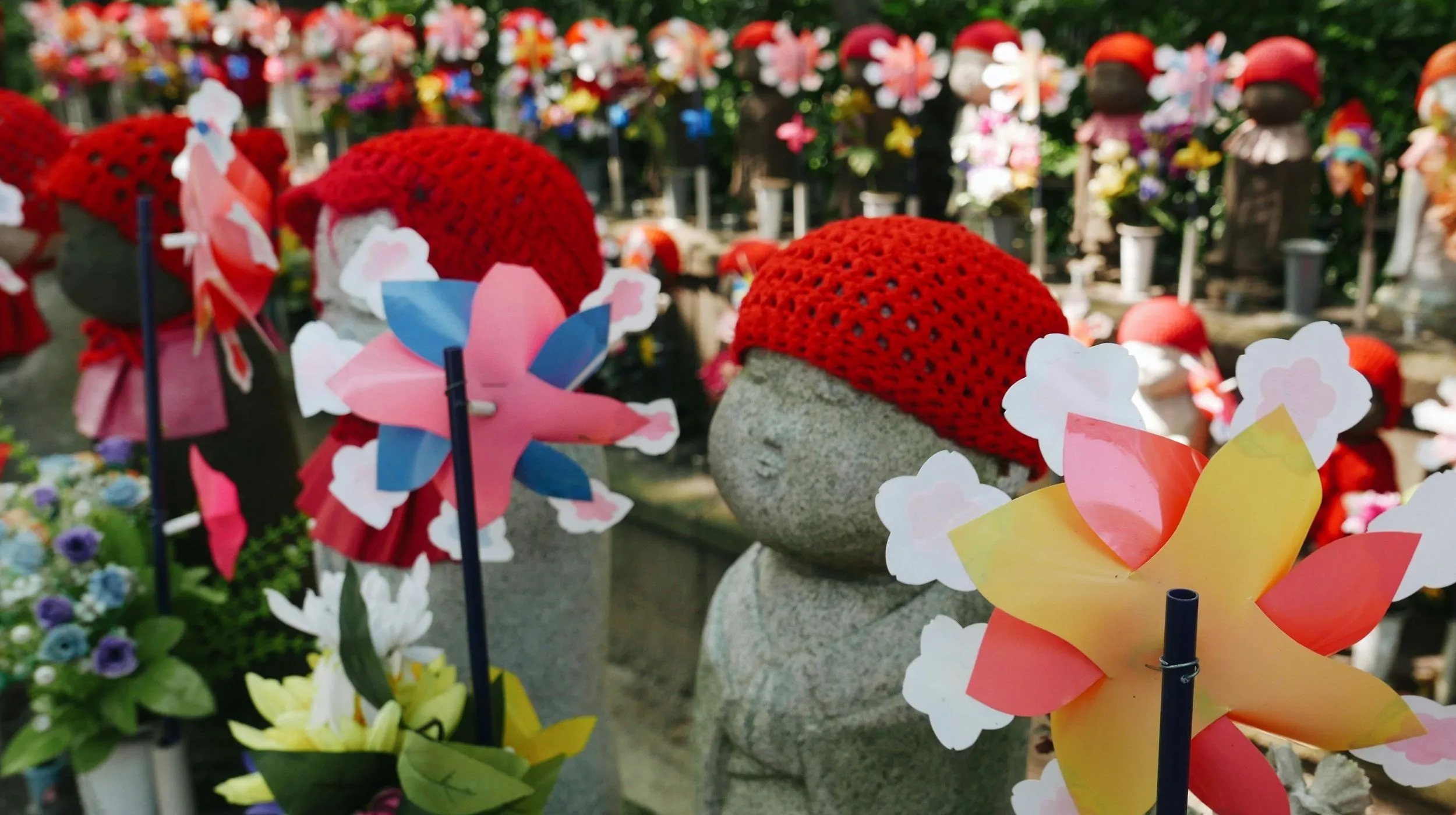 Japon — Statues mignonnes ornées de chapeaux rouges entourées de fleurs colorées dans un cadre paisible.
