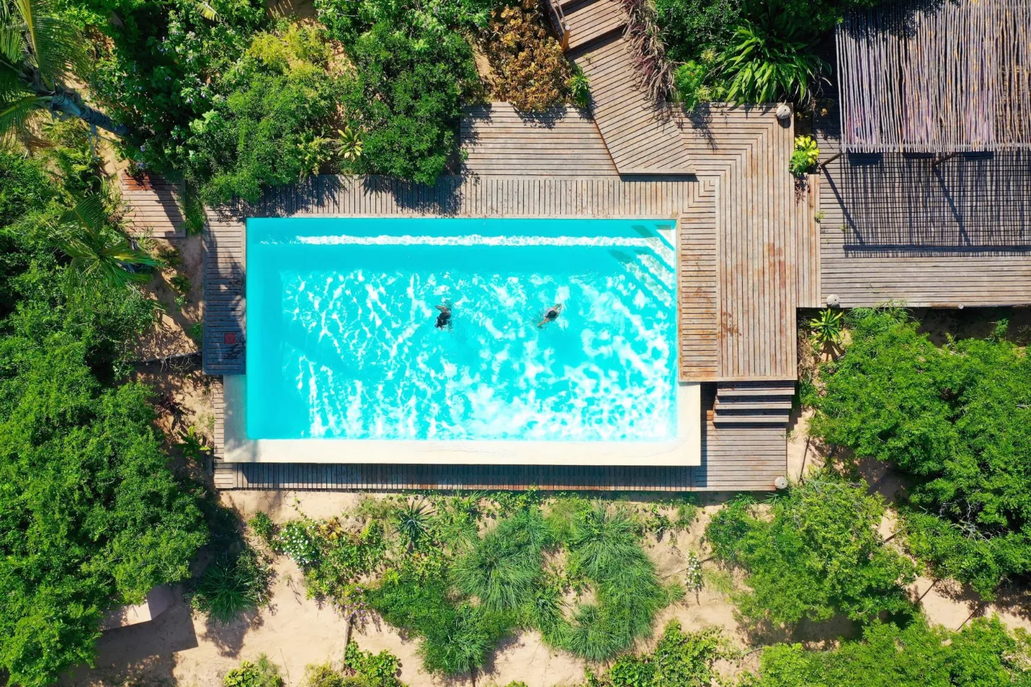 Piscine turquoise entourée de verdure luxuriante et de terrasses en bois, idéale pour une escapade paisible.