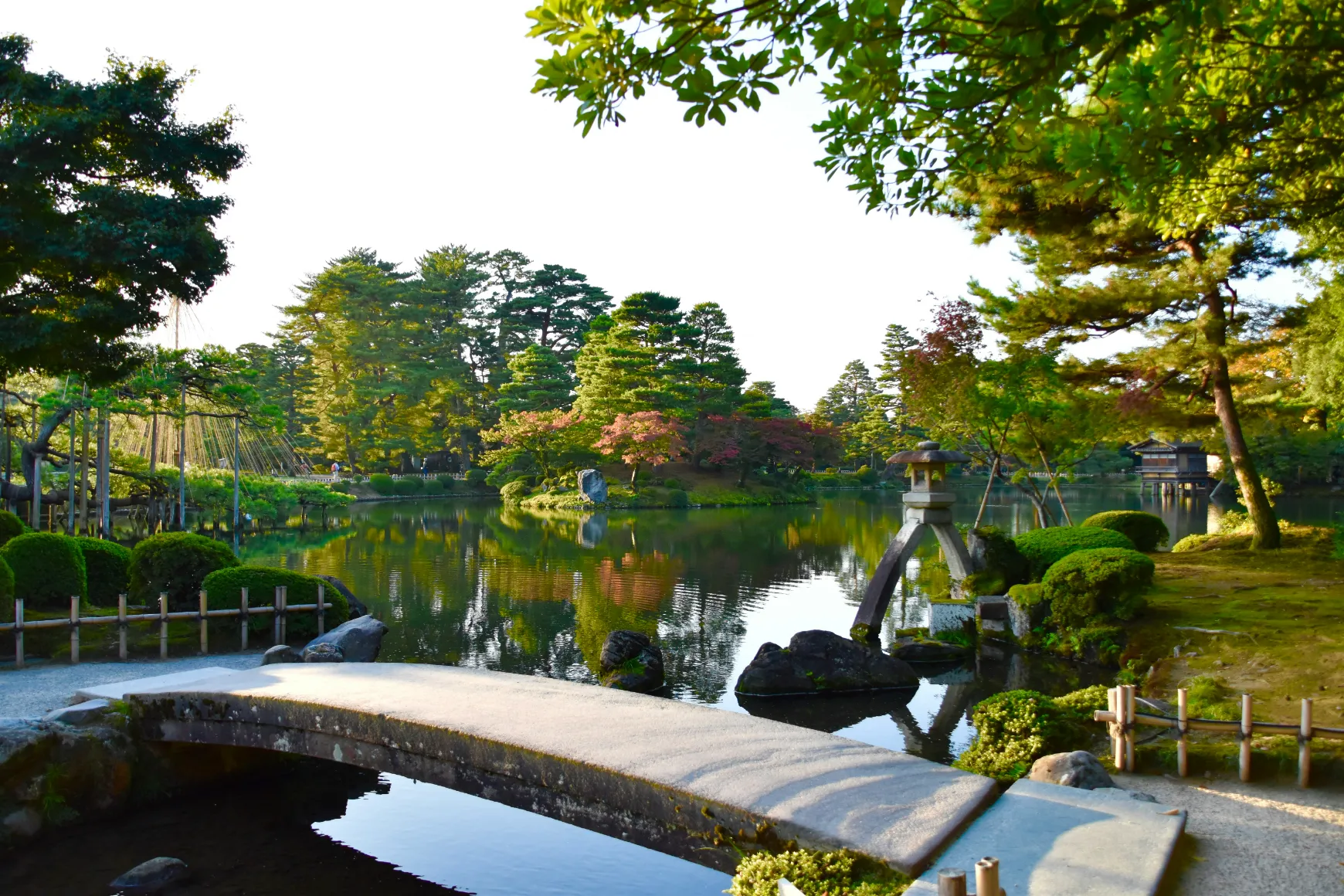 Japojn - Jardin paisible et luxuriant avec un étang, des arbres majestueux et un pont en pierre invitant à la contemplation.