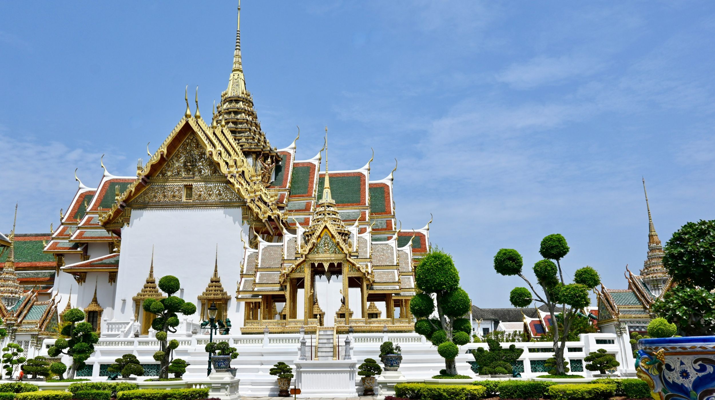 Bangkok, Thaïlande — majestueux temple doré entouré de jardins luxuriants sous un ciel bleu éclatant.