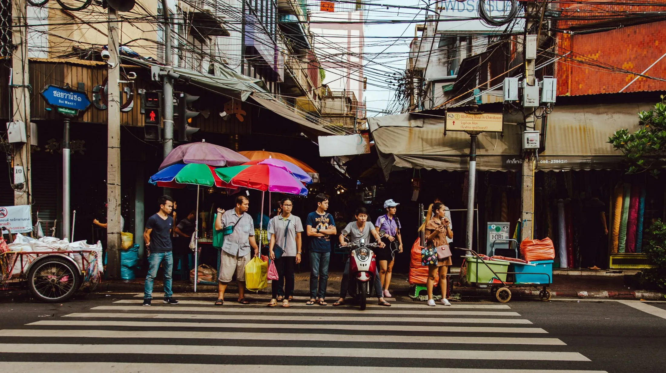 Scène animée de rue avec des piétons et des parasols colorés sous un ciel lumineux, Thaïlande.
