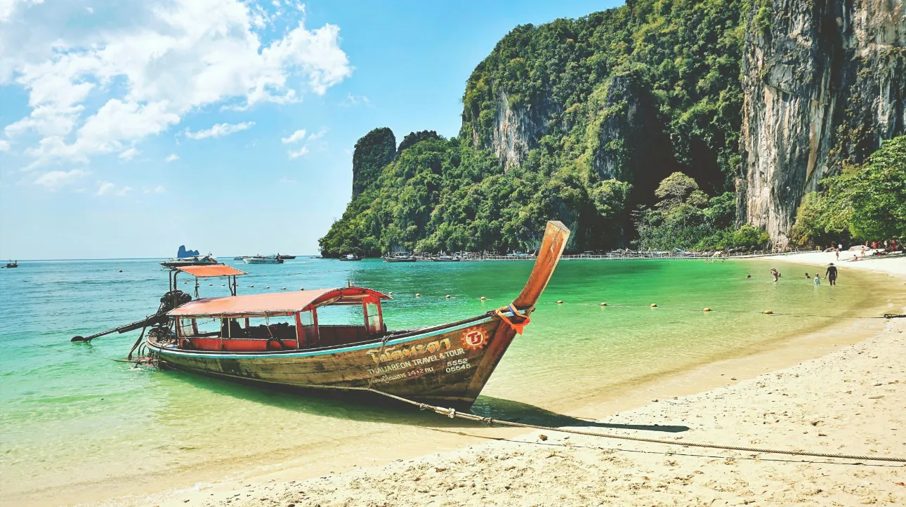 Plage idyllique en Thaïlande avec un bateau traditionnel et des eaux cristallines.