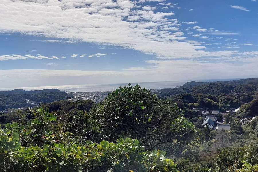 Vue panoramique sur une vallée verdoyante, avec un ciel lumineux et quelques nuages épars.