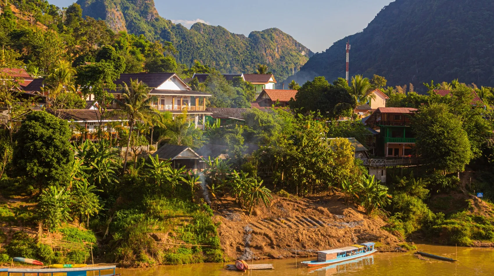 Village pittoresque au bord de la rivière, entouré de montagnes verdoyantes et de végétation luxuriante.