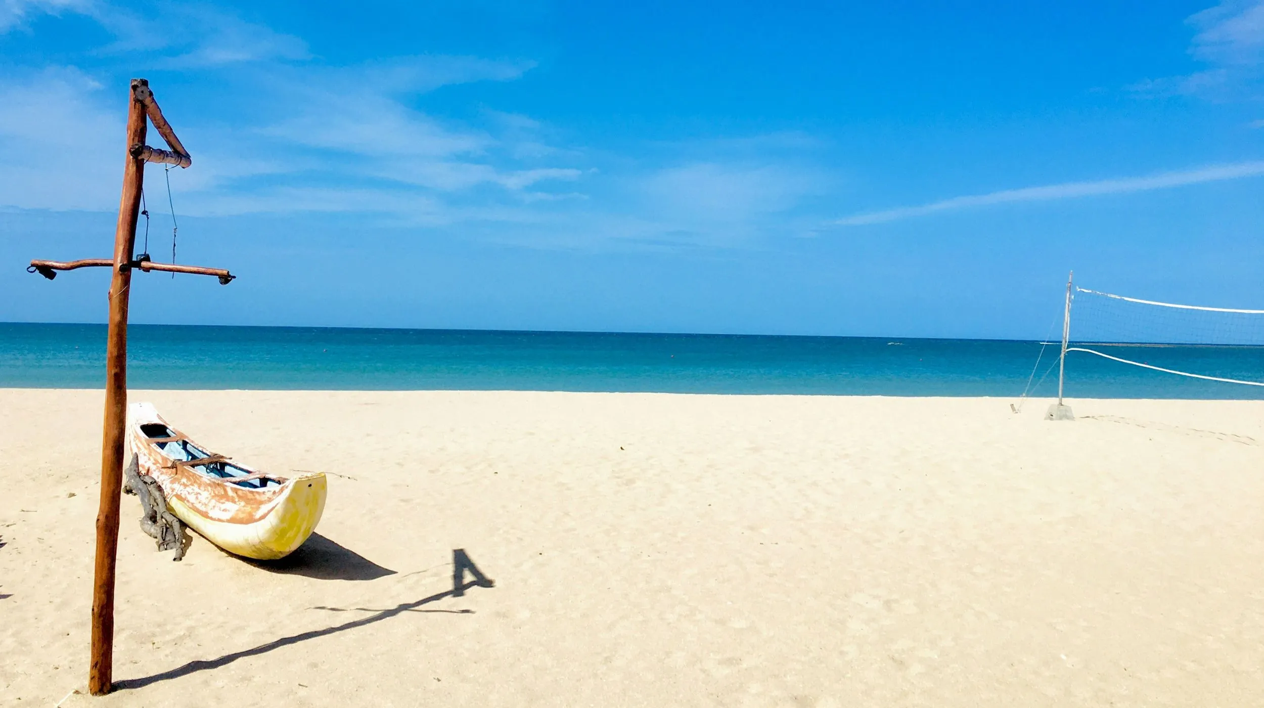 Plage paisible avec un bateau en bois, ciel bleu éclatant et mer turquoise, invitant à la détente.