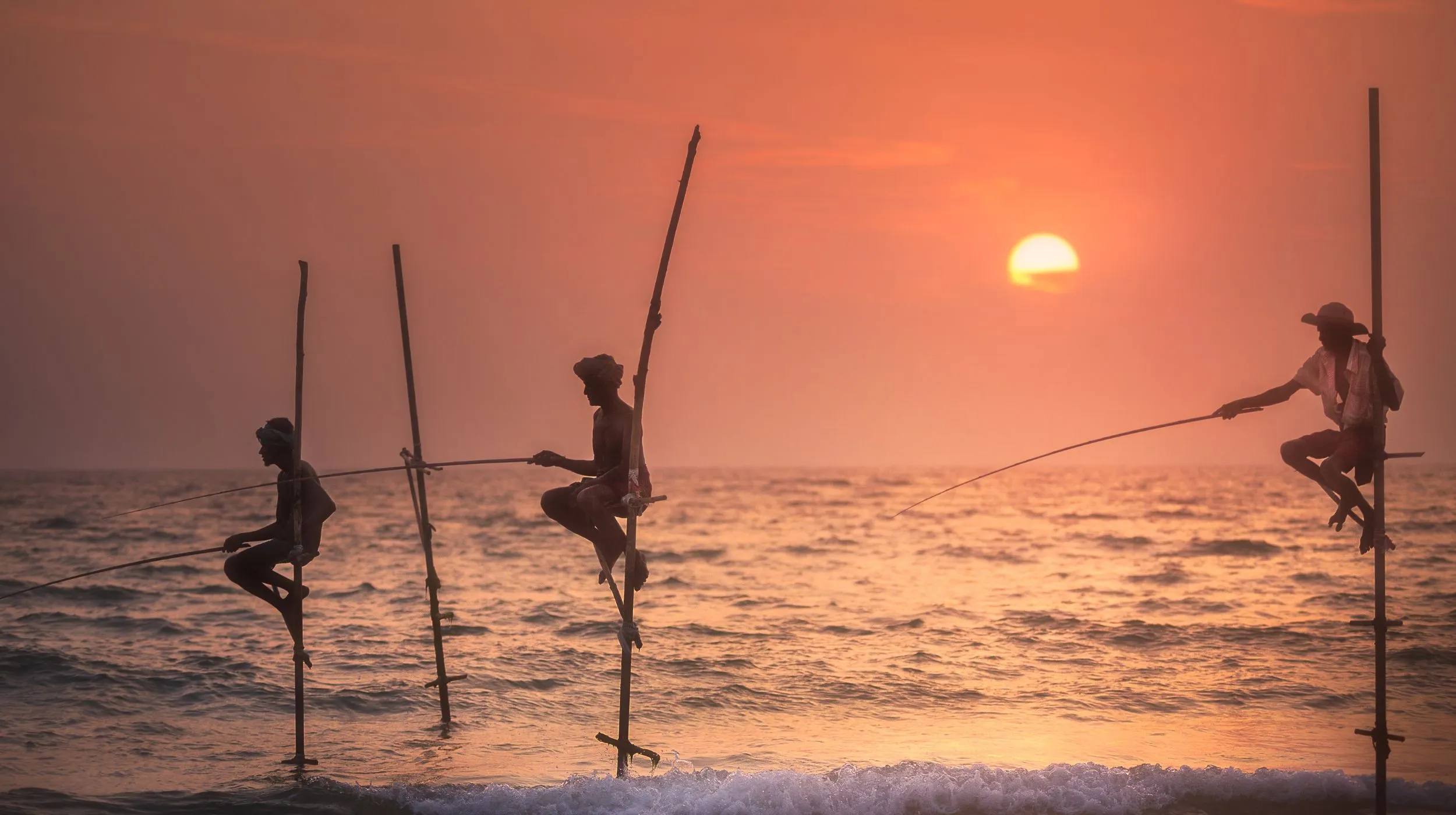 Pêcheurs perchés sur des poteaux au coucher du soleil — scène envoûtante et authentique au bord de l'océan.