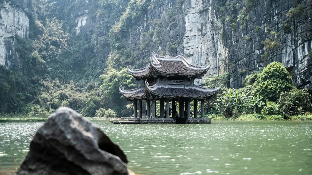 Temple paisible sur l'eau, entouré de falaises verdoyantes et de végétation luxuriante.