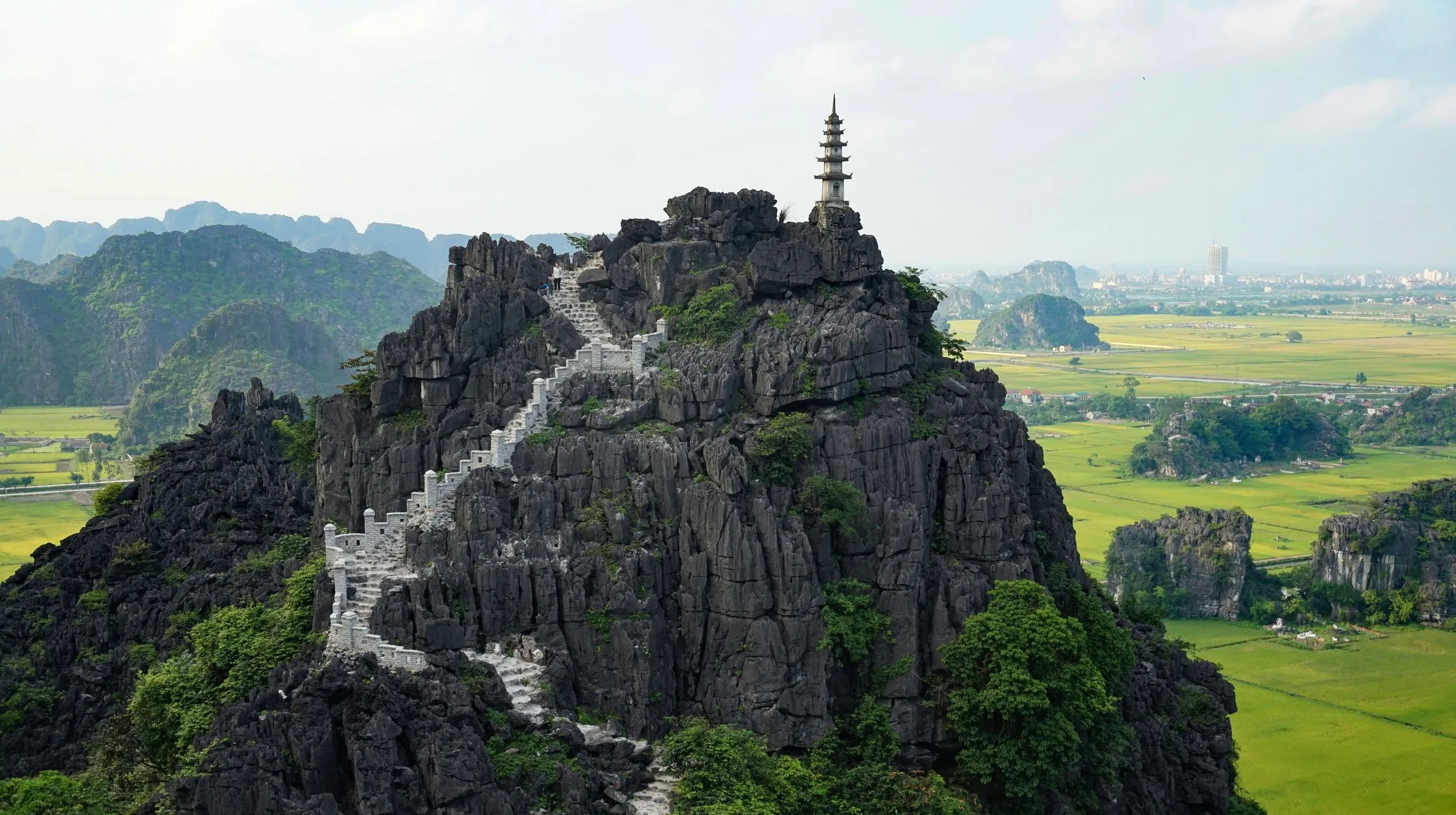 Roc majestueux surplombant des rizières verdoyantes, offrant une vue spectaculaire sur un paysage enchanteur.