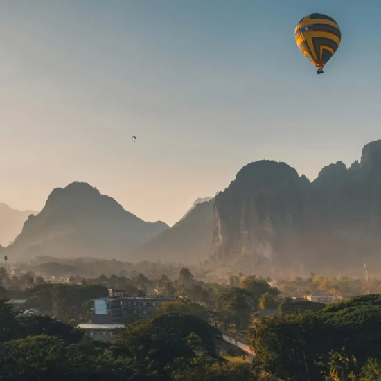 Montagnes majestueuses au lever du soleil, survolées par une montgolfière colorée dans un paysage enchanteur.