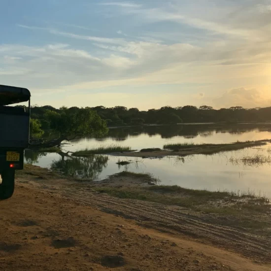 Coucher de soleil sur un paisible plan d'eau, avec un véhicule garé sur une route de terre.